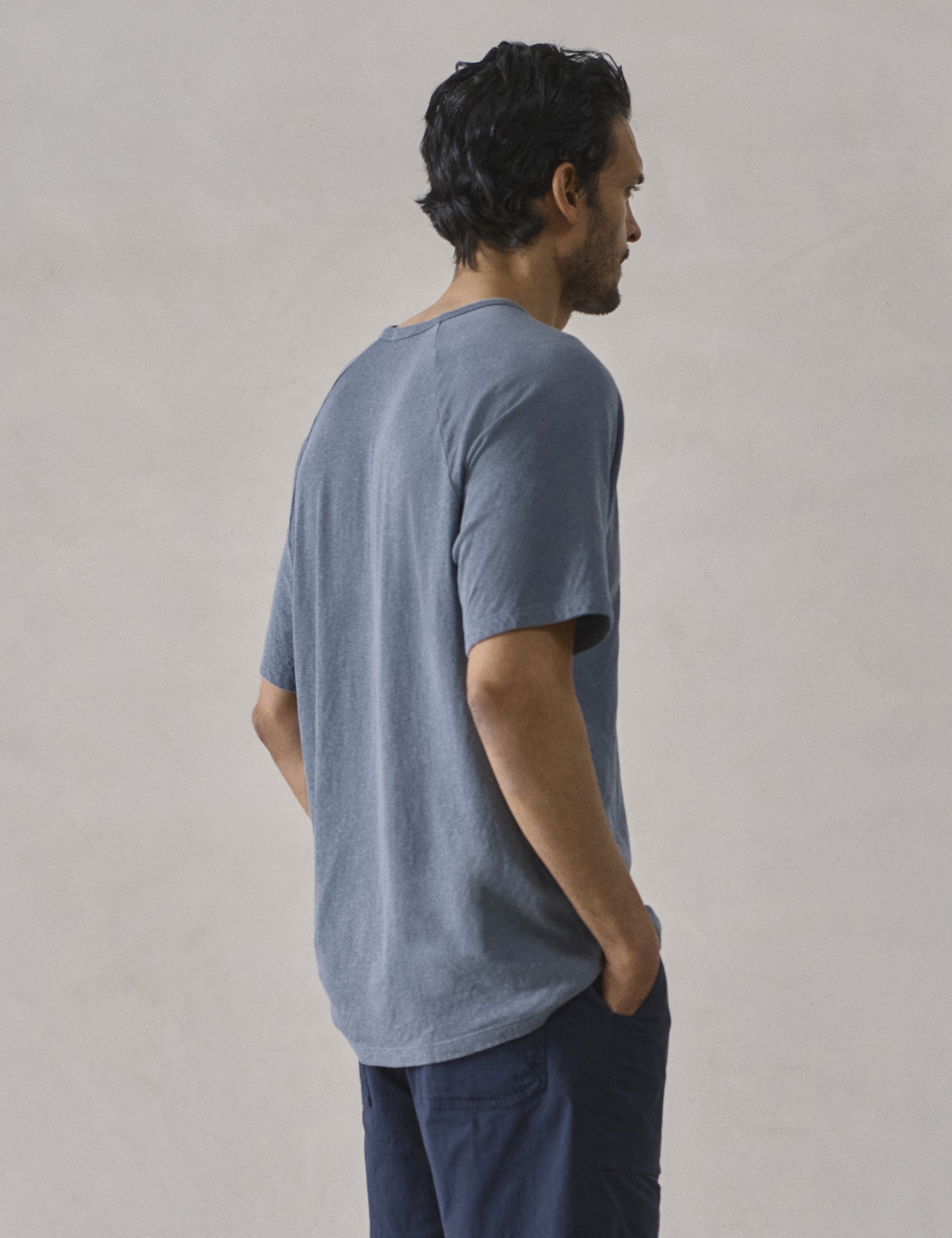 Rear 3/4 upper-body view of man wearing Buckhorn Cotton Raglan Tee 2.0 in Portal Blue from AETHER Apparel.