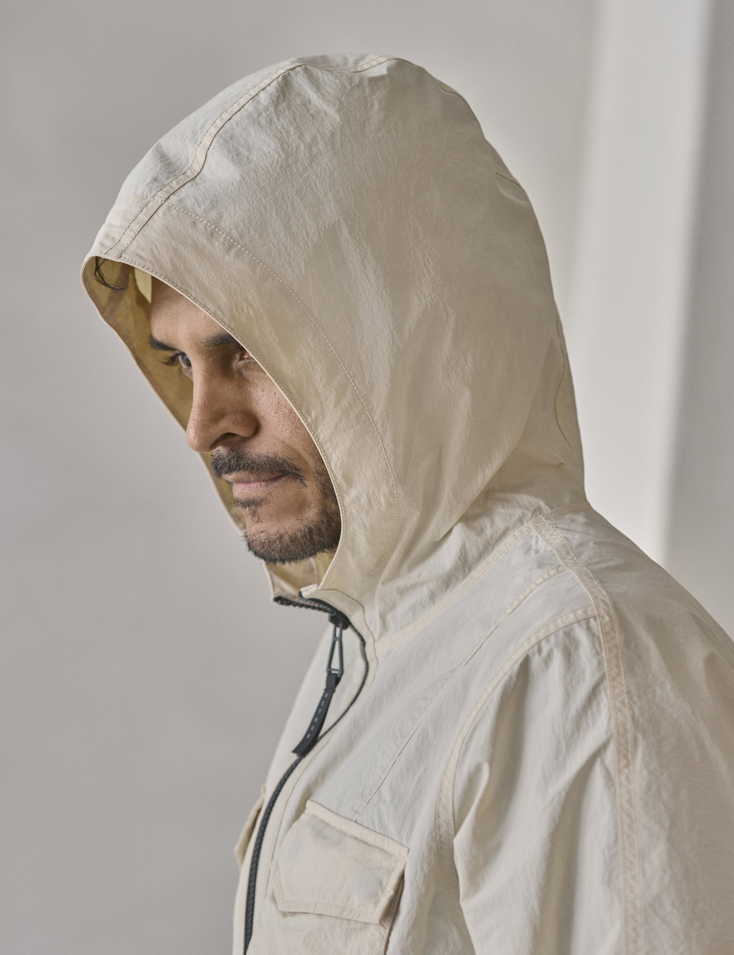 Studio image of man wearing the three-piece hood on the Aires Lightweight Windbreaker in Bone white from AETHER Apparel.
