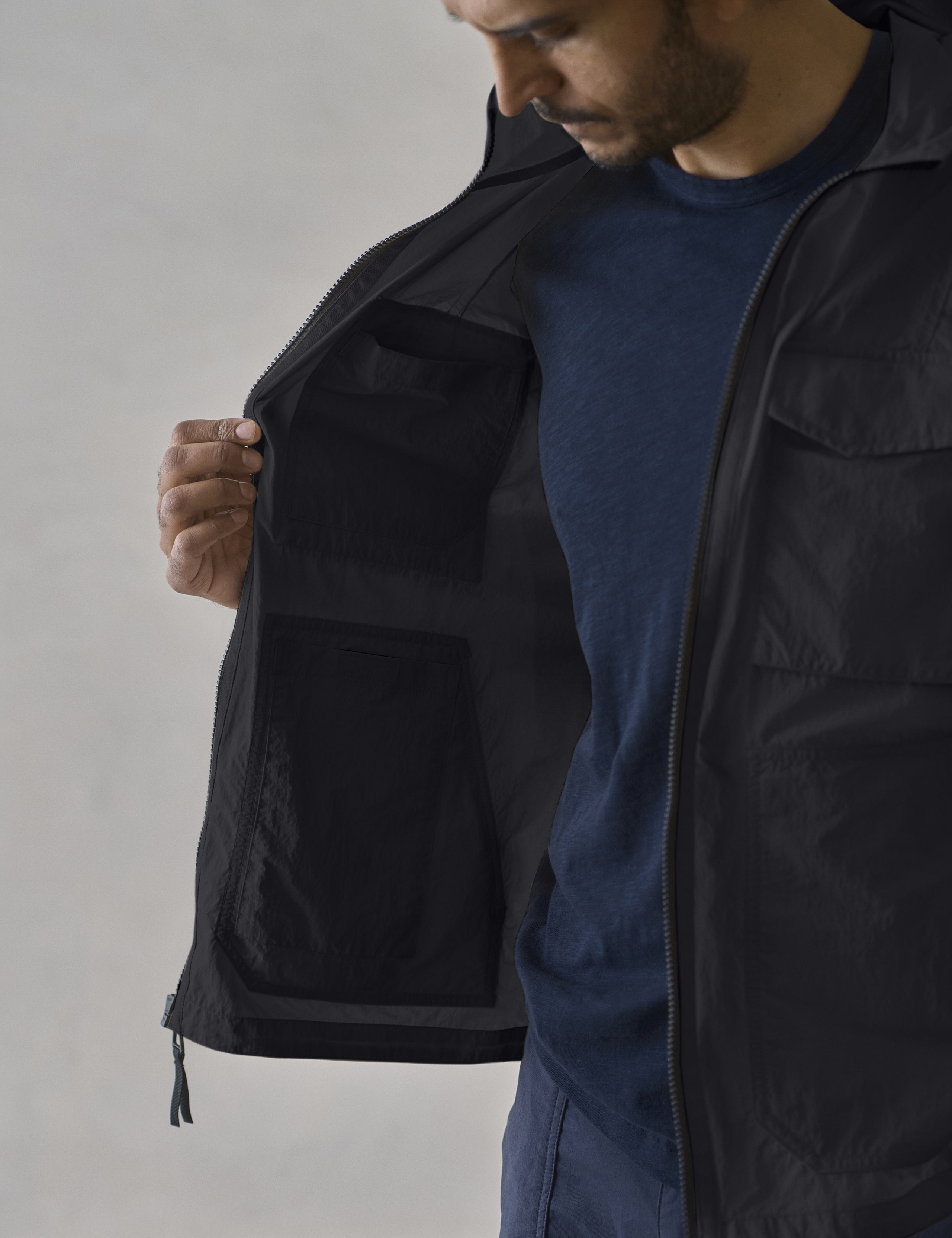 Studio image of man holding open the Aires Lightweight Windbreaker in Onyx Black from AETHER Apparel, showing off the interior pockets. 