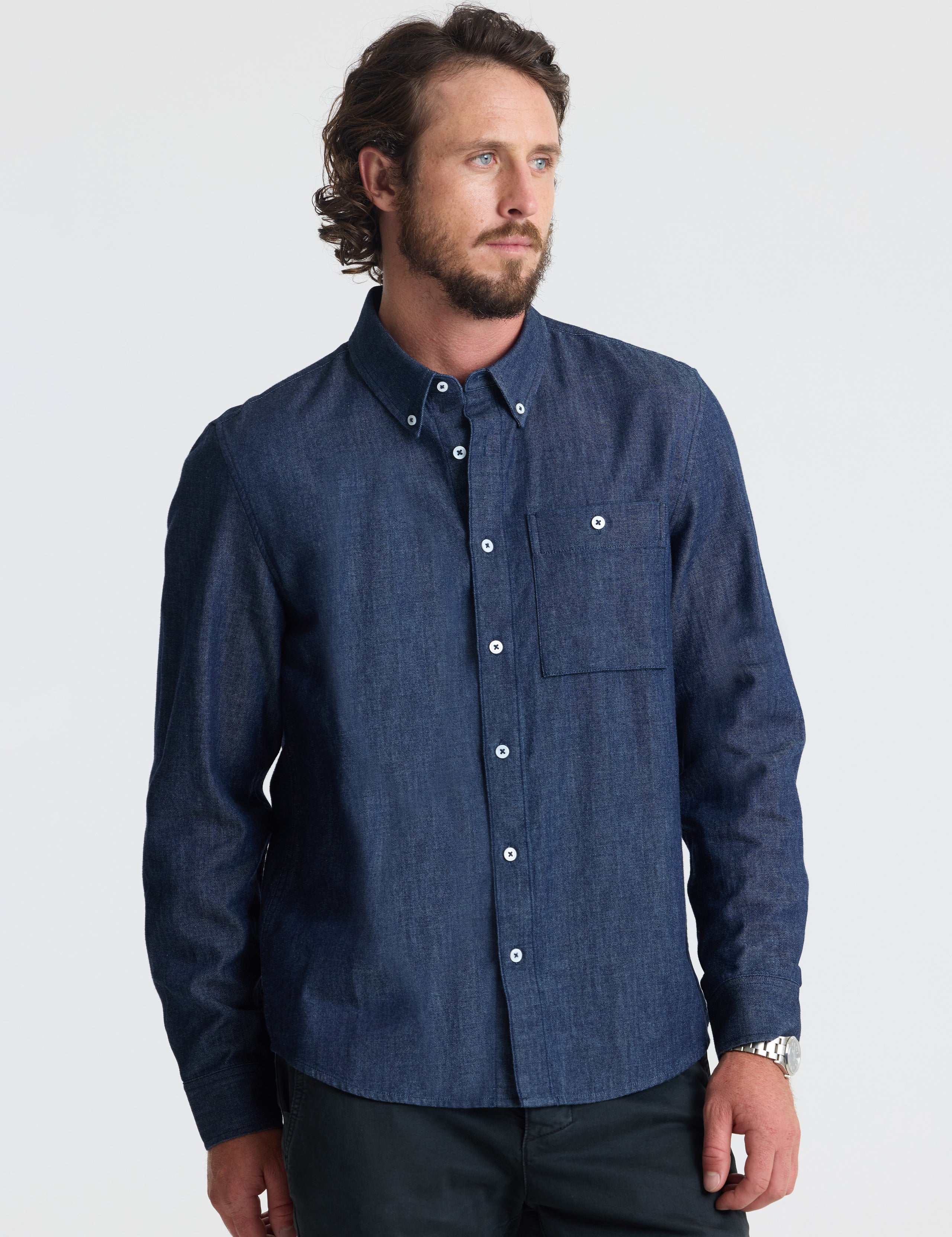 Angled view of man wearing Alder Chambray Button-Down in Dark Blue from AETHER Apparel.
