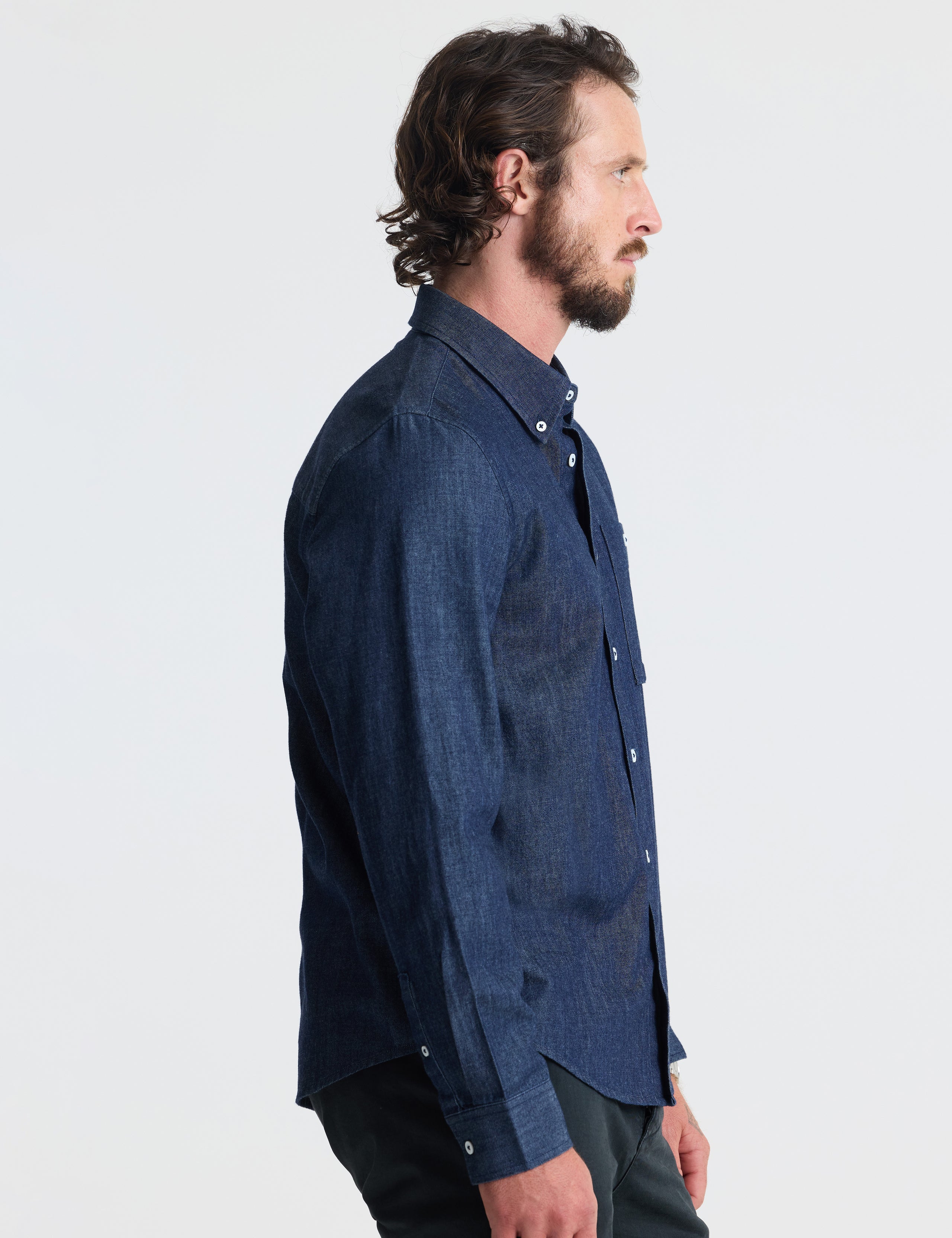 Side profile of man wearing Alder Chambray Button-Down in Dark Blue from AETHER Apparel.