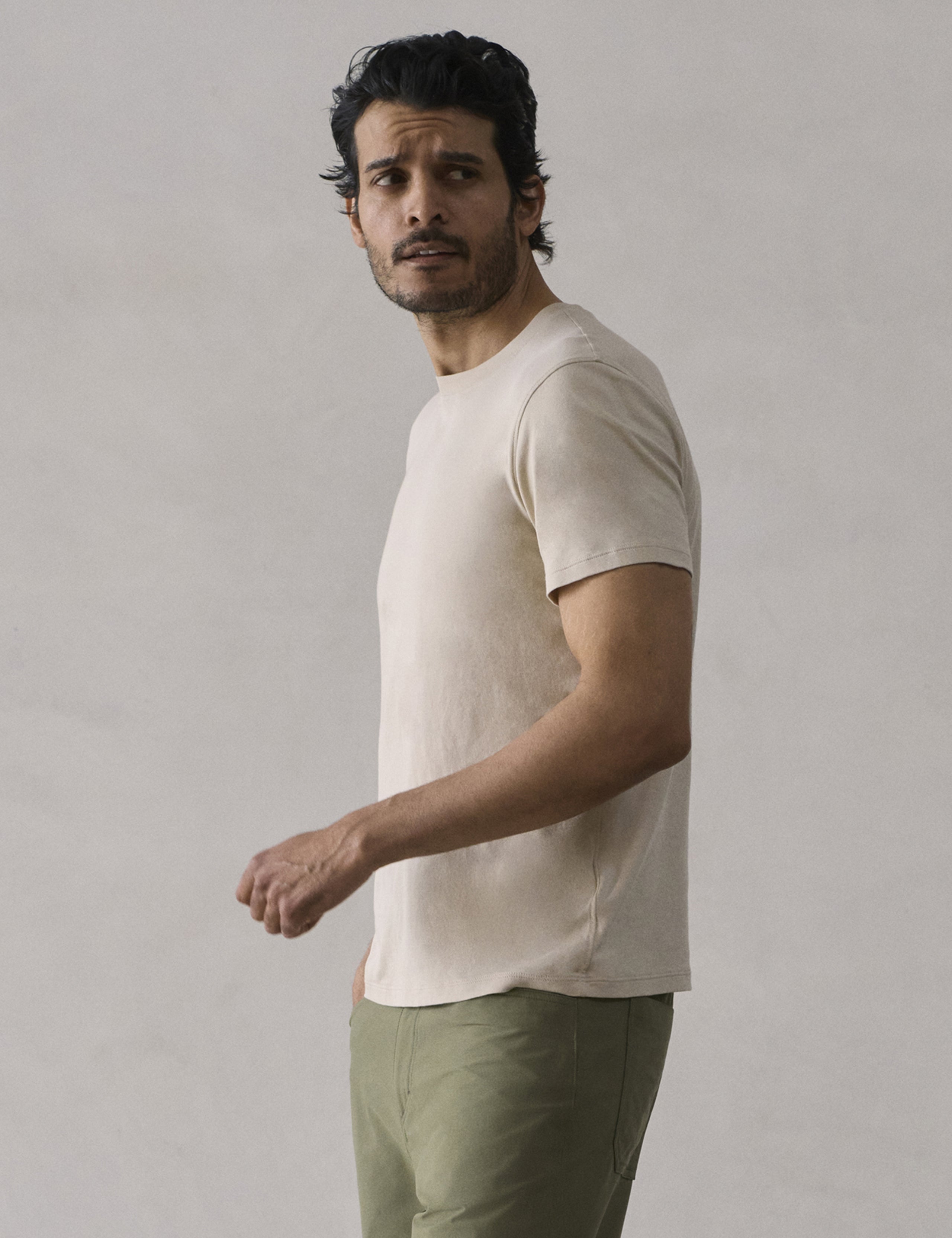 Side profile view of man wearing Emery Pima Crew Tee in Bone white from AETHER Apparel.