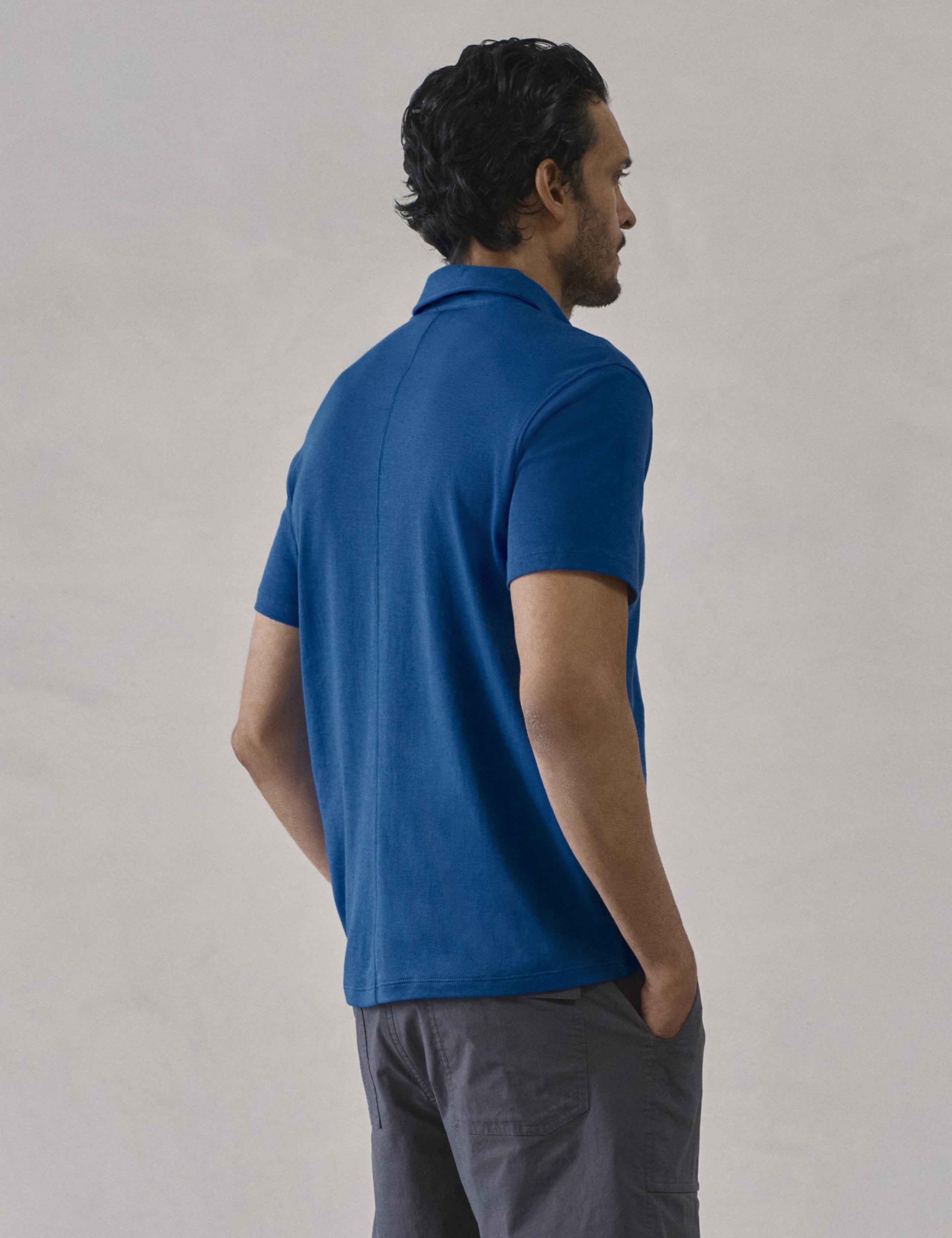 Rear 3/4 view of man wearing Emery Pima Polo in Summit Blue from AETHER Apparel.