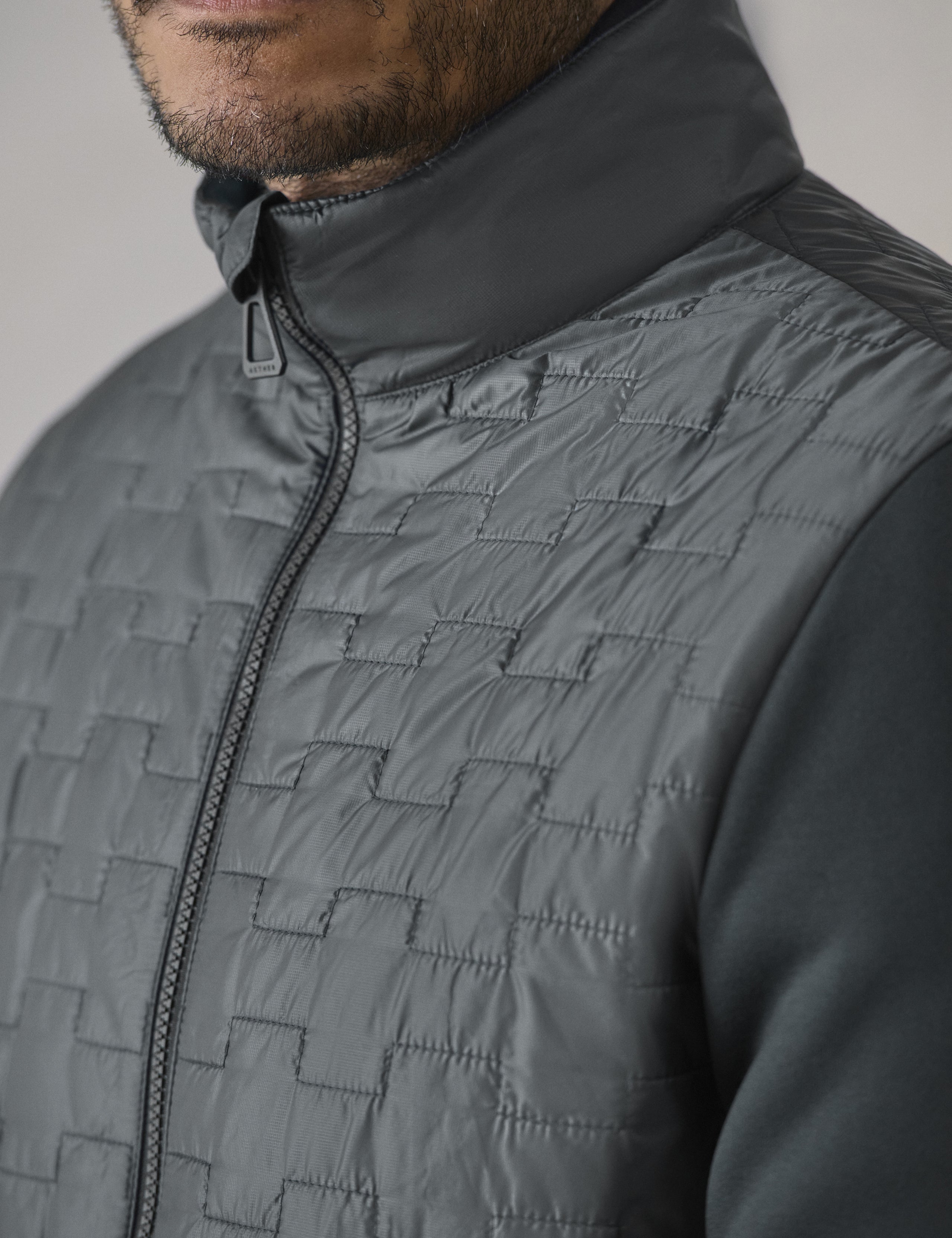 Closeup detailed view of the main center-front zipper, collar, and micro ripstop custom quilted body on the Hybrid Tech Full-Zip in Graphite from AETHER Apparel.