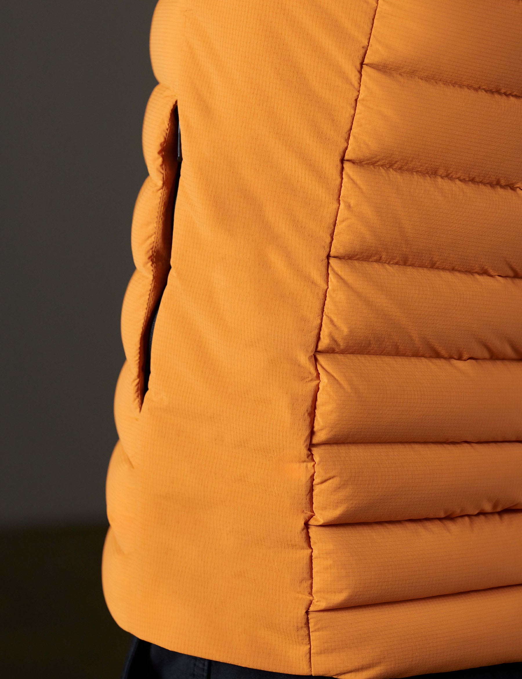 Closeup detailed view of the exterior baffling and left hand pocket on the Launch Vest in Midas Orange from AETHER Apparel.