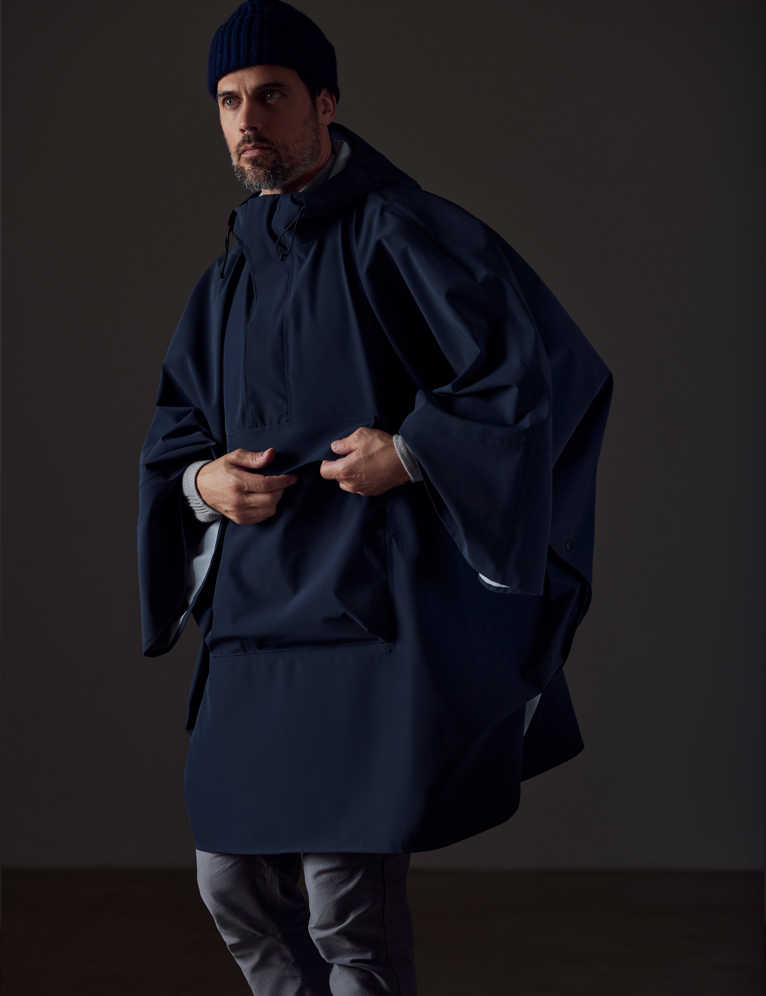 Front angled view of man wearing the Line Poncho in Total Eclipse dark blue from AETHER Apparel, highlighting front drop pocket.