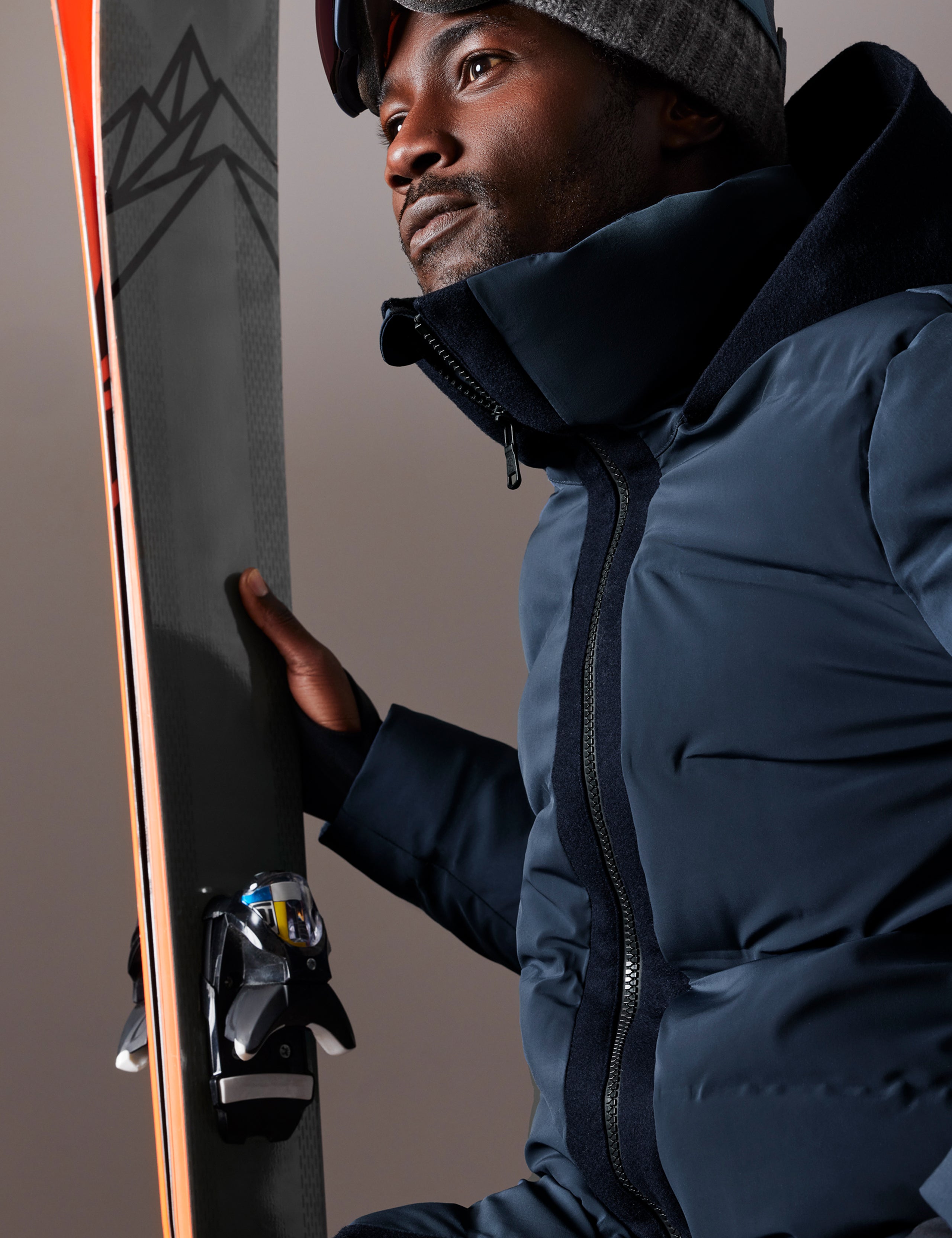 Front 3/4 body view of man holding skis in hand wearing Nordic Jacket in Total Eclipse dark blue from AETHER Apparel.