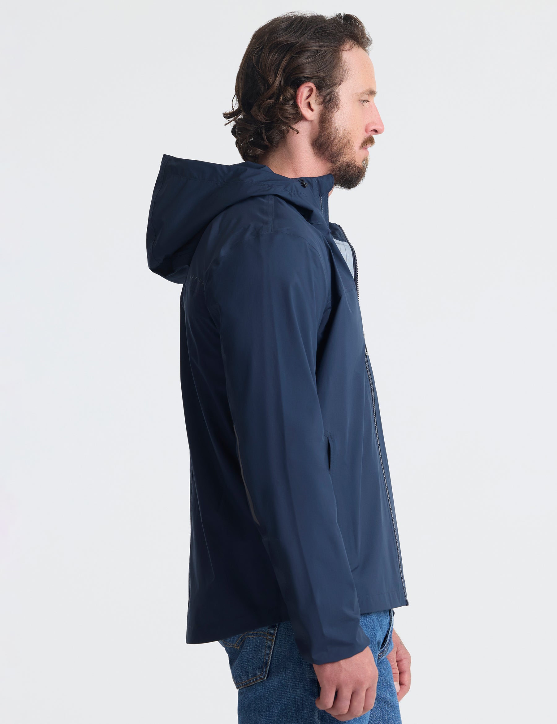 Right profile view of man wearing Storm All-Weather Jacket in Total Eclipse dark blue from AETHER Apparel.
